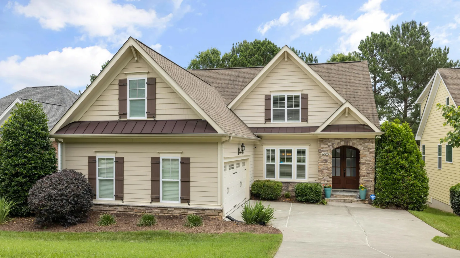 Tan home with brown shingle roof and stone arched entryway