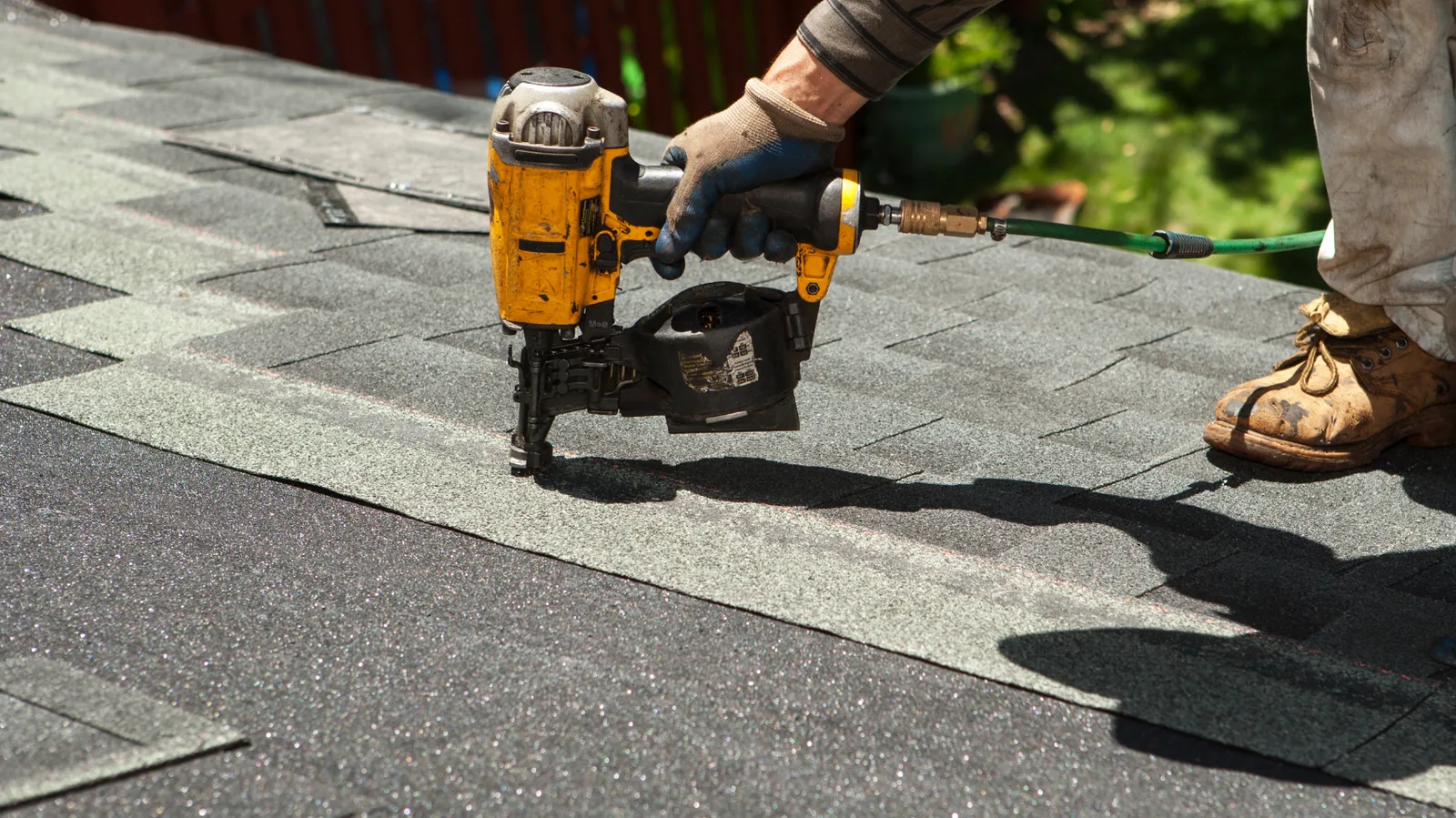 A roofer using a nail gun to secure roof shingles